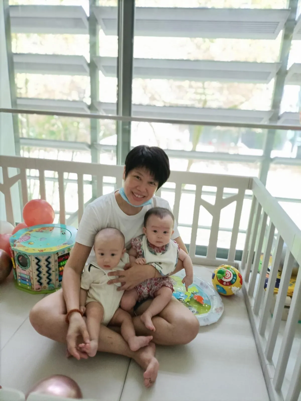 Photo: May Leng sitting in a playpen with two baby twins